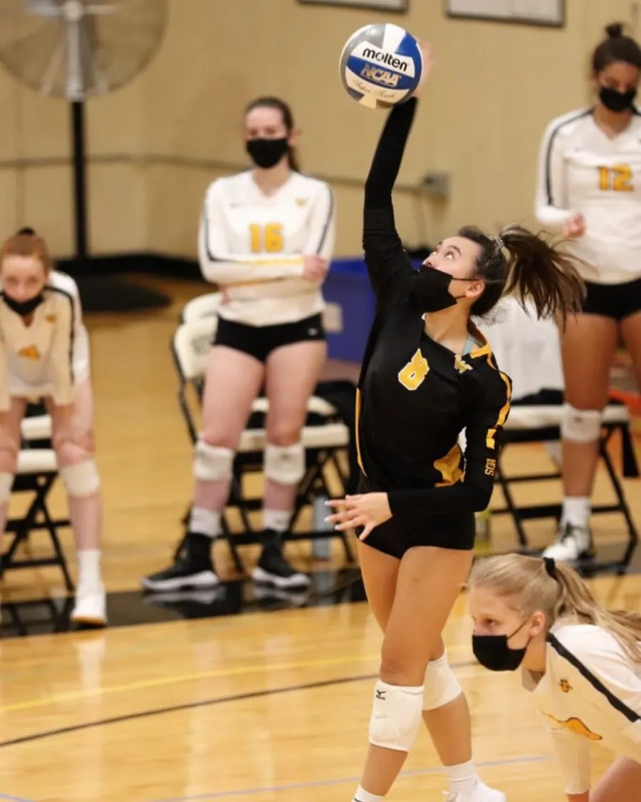 A high-school volleyball player rising to attack the ball at the net during a match.