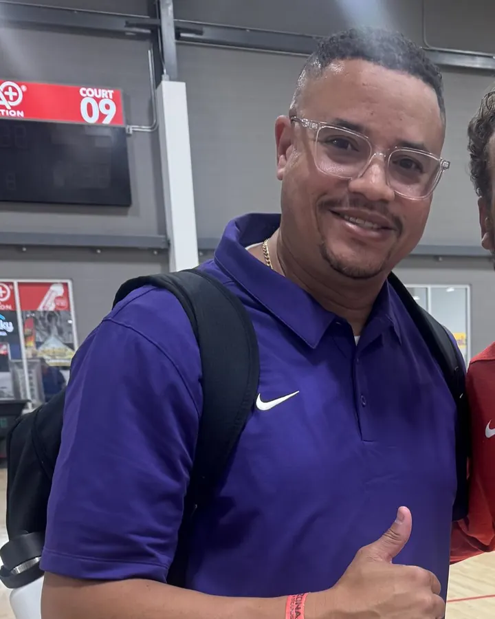 Kiyoshi "Coach Fish" Fish, wearing a purple polo shirt, at a basketball tournament venue.