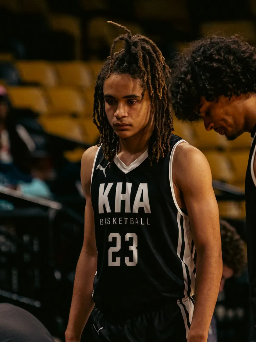 A high-school basketball player in a KHA Basketball number 23 jersey standing courtside during a game.